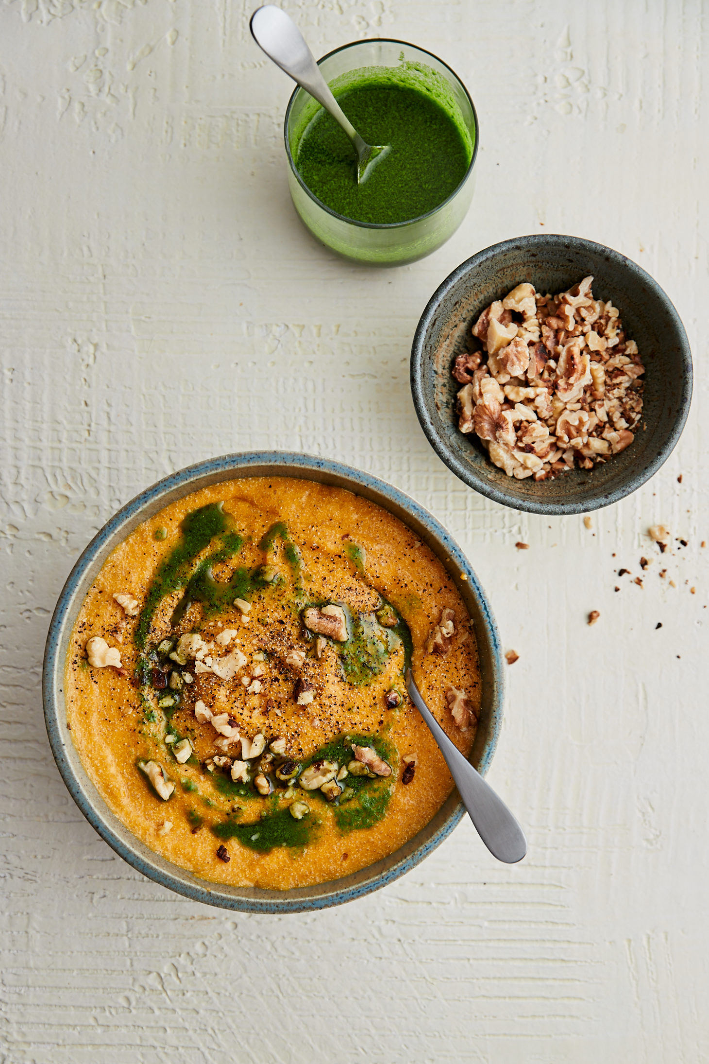 Blue bowl with carrot polenta on a white background with parsley oil and walnuts.