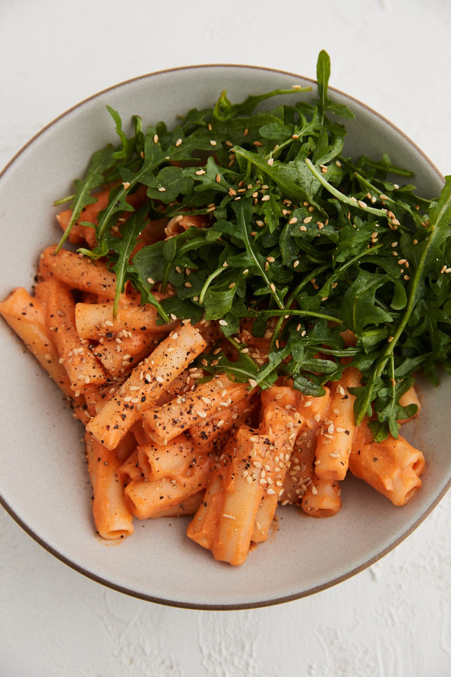 Close-up image of pasta topped in a carrot sauce and arugula.