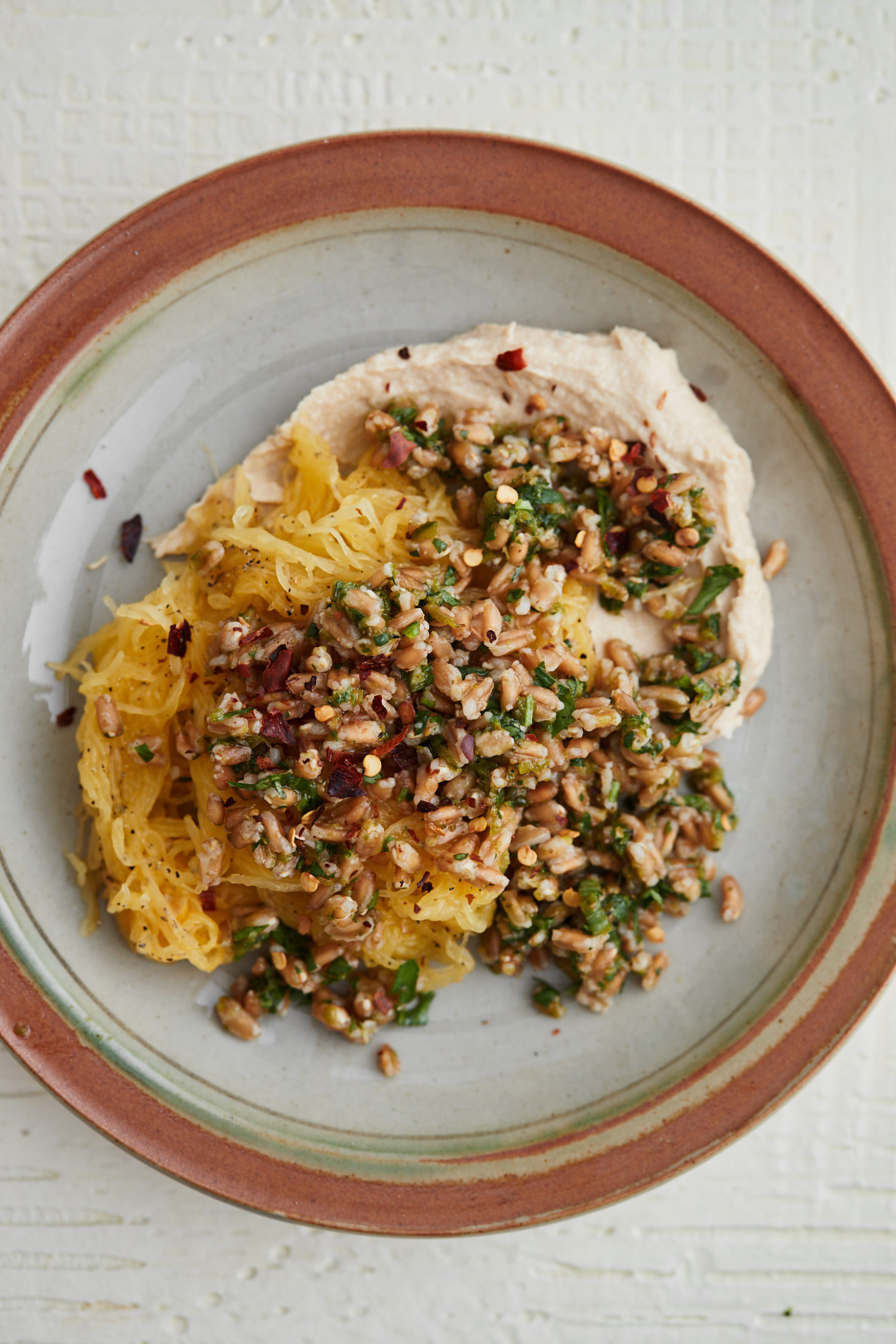 A grey plate with brown rim topped with hummus, spaghetti squash, and farro.