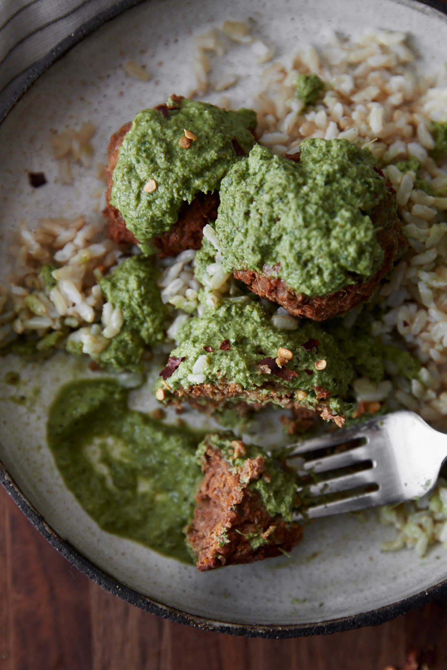 close-up of a cream bowl with green broccoli pesto with lentil bites and rice.