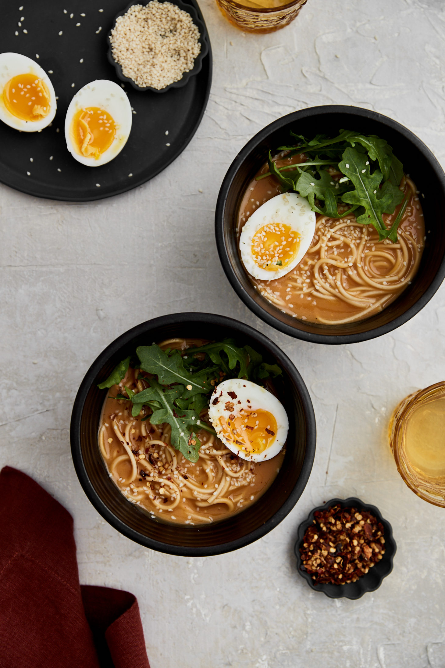 two black bowls of noodles in broth topped with arugula and cut-open soft-boiled eggs.