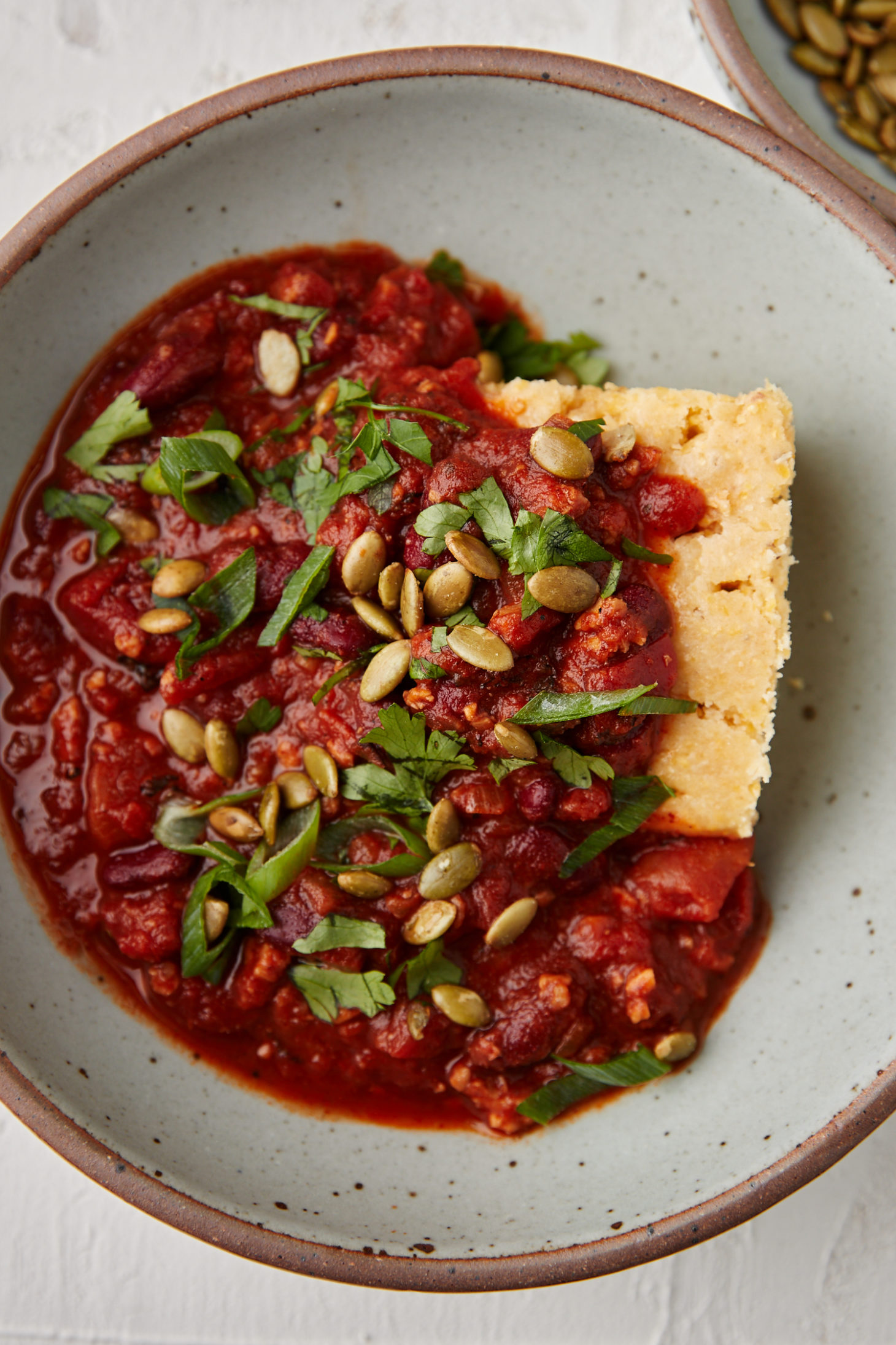 Close-up photo of tempeh chili smothered a piece of cornbread in a grey bowl.