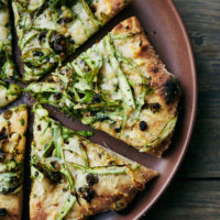 Close-up of asparagus pizza cut into pieces on a red plate.