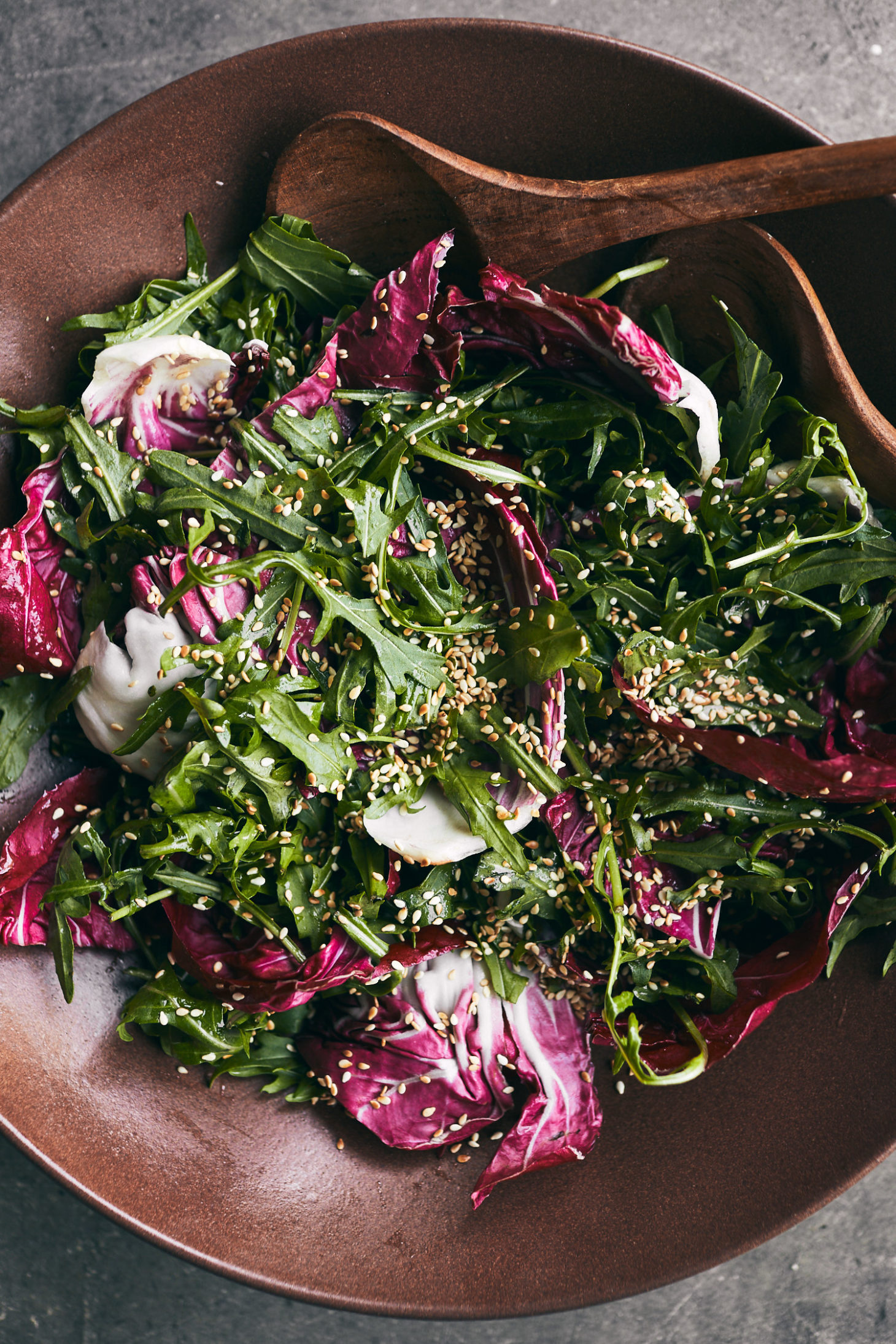 close-up of a brick colored bowl filled with arugula, radicchio, and sesame seeds.