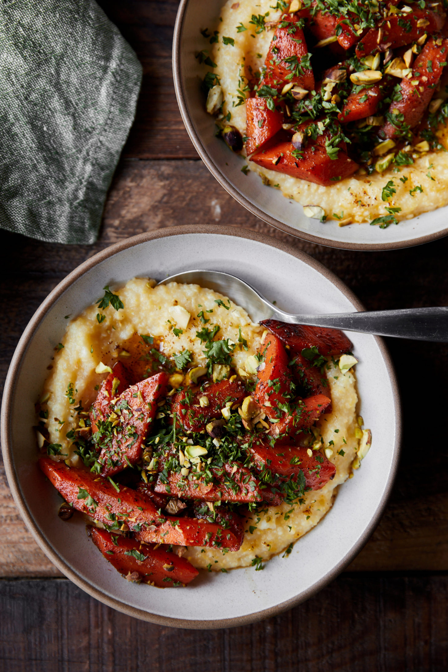 two white bowls of yellow polenta topped with orange braised carrots