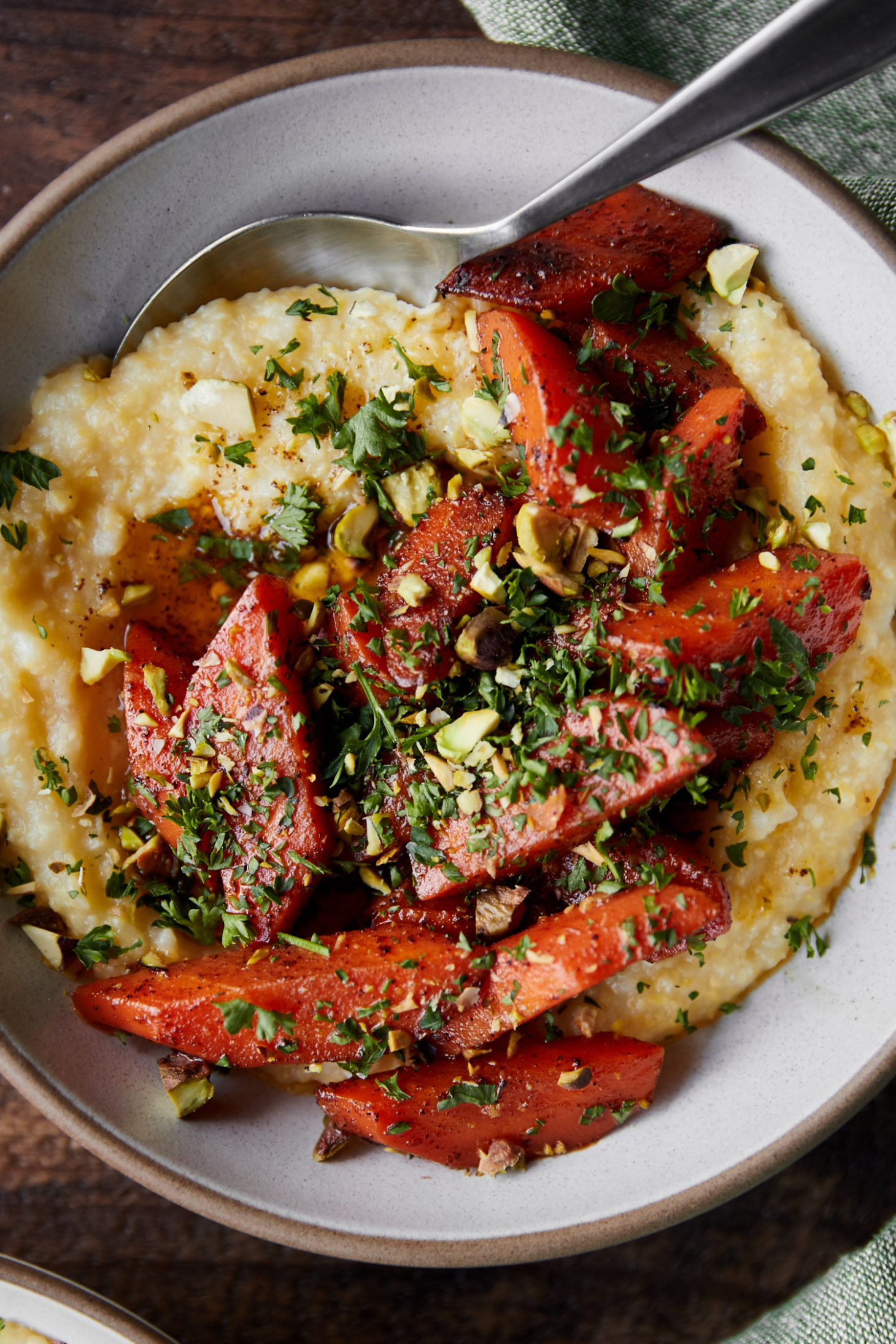 Close-up image of a white bowl with polenta and topped with orange braised carrots.