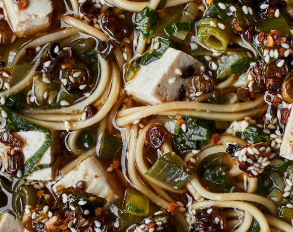Close-up image of noodles and tofu in a tan broth, scallions, and bok choy