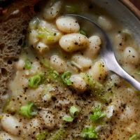 Close-up of white beans in their broth with thinly sliced green scallions and black pepper on top.