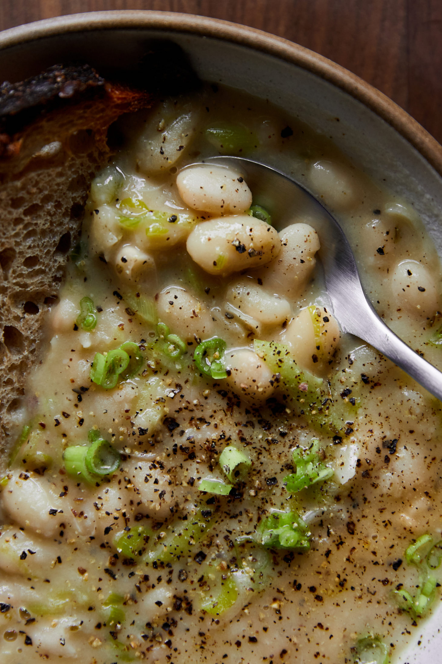 Close-up of white beans in their broth with thinly sliced green scallions and black pepper on top.
