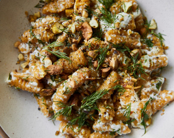 Close-up photo of orange cavatelli in a white bowl topped with ricotta and dill.