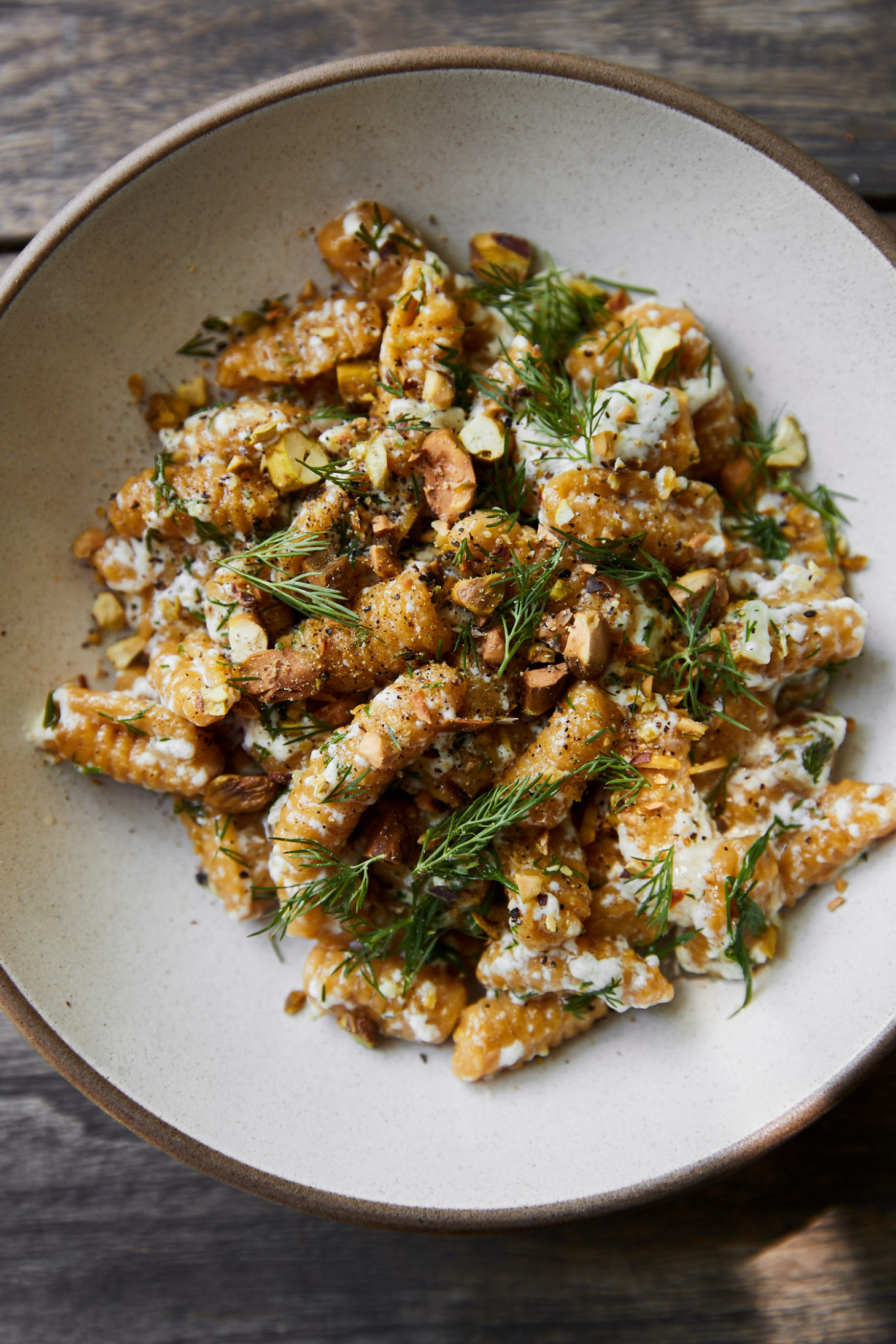 Close-up photo of orange cavatelli in a white bowl topped with ricotta and dill.