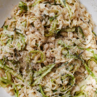 Close-up photo of pasta in a braiser tossed with shaved asparagus, white beans, basil, and parmesan
