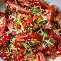 Close-up photo of tomato salad with fresh scallions in a bowl with blue speckles.