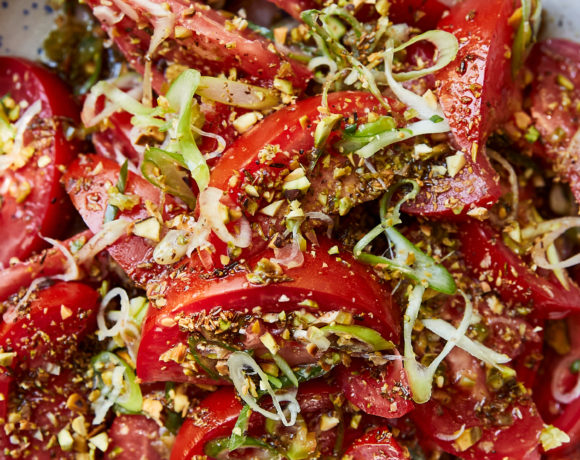 Close-up photo of tomato salad with fresh scallions in a bowl with blue speckles.