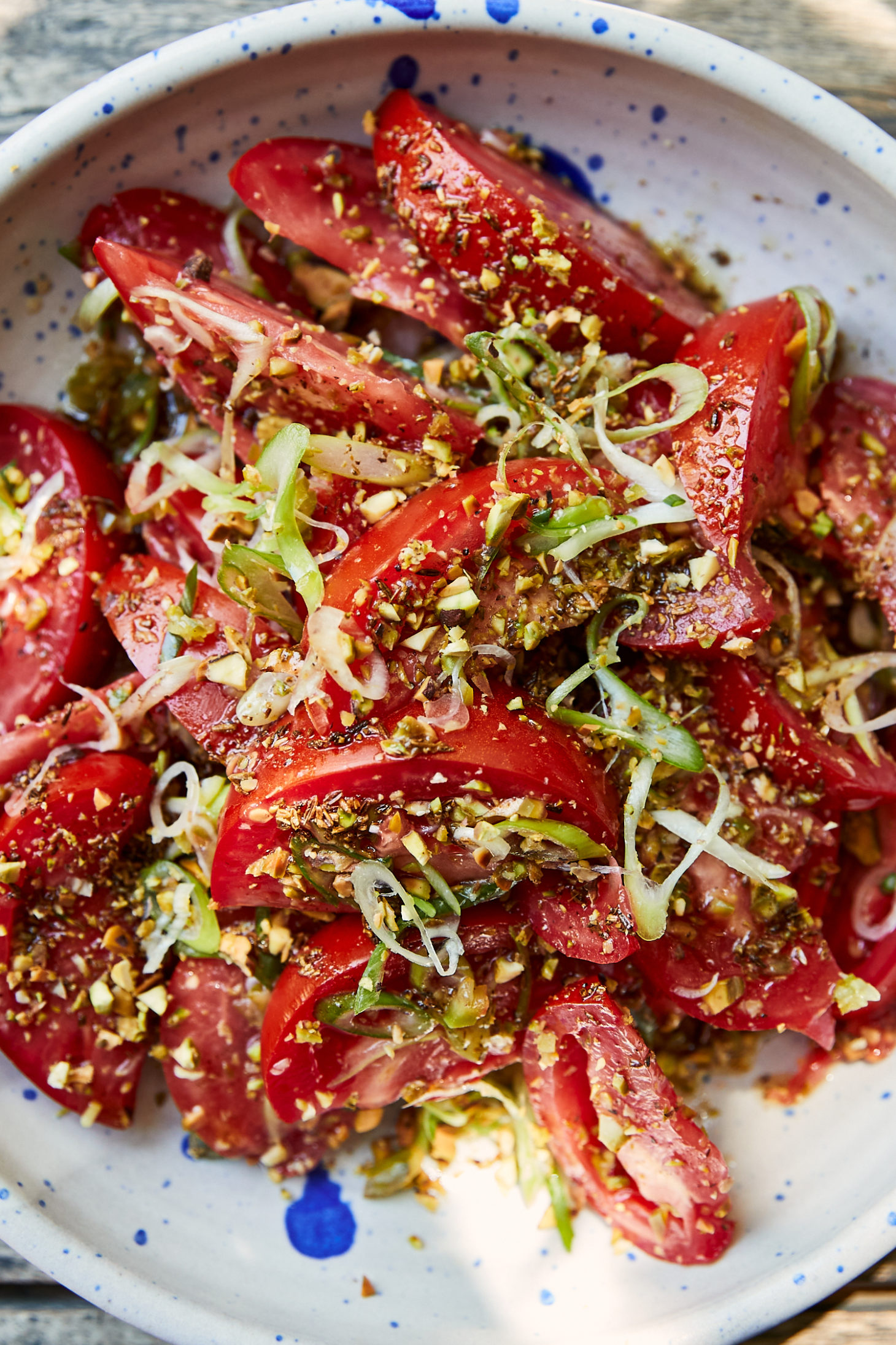 Close-up photo of tomato salad with fresh scallions in a bowl with blue speckles.