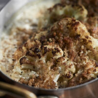 Close-up on a small copper roasting pan filled with toasted cauliflower cooked in heavy cream.