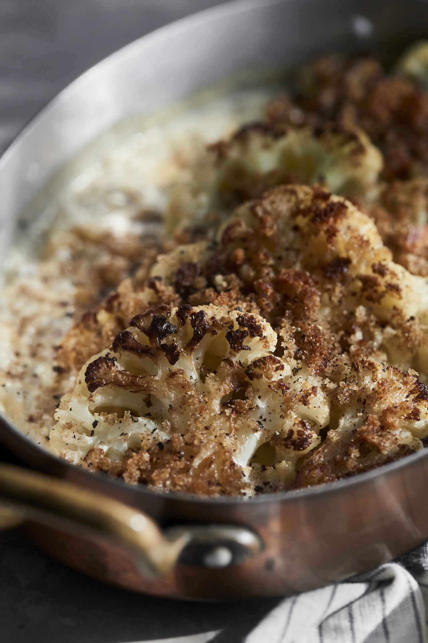 Close-up on a small copper roasting pan filled with toasted cauliflower cooked in heavy cream. 