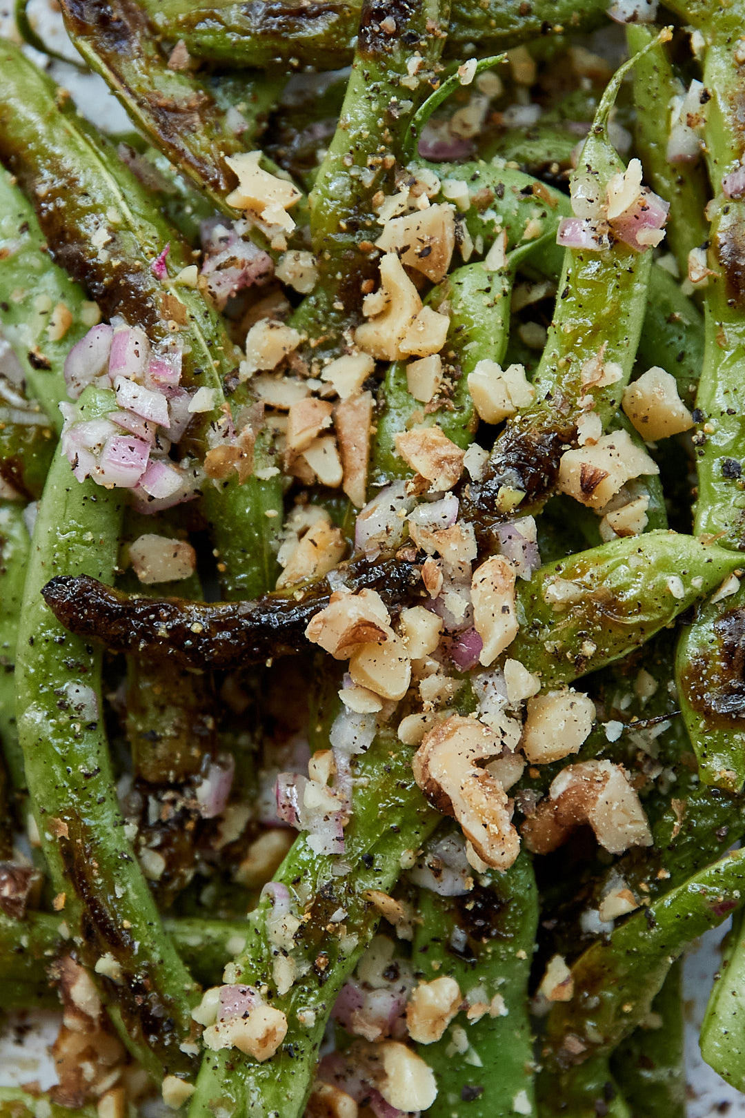 Close-up of charred green beans topped with black pepper, minced red onion, and finished with crushed walnuts.
