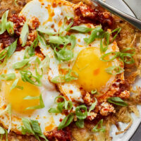 Close-up photo of crispy hash browns covering a plate, topped with a chile fried egg.