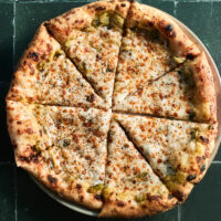 A full overhead photo of zucchini pizza on a green tile background
