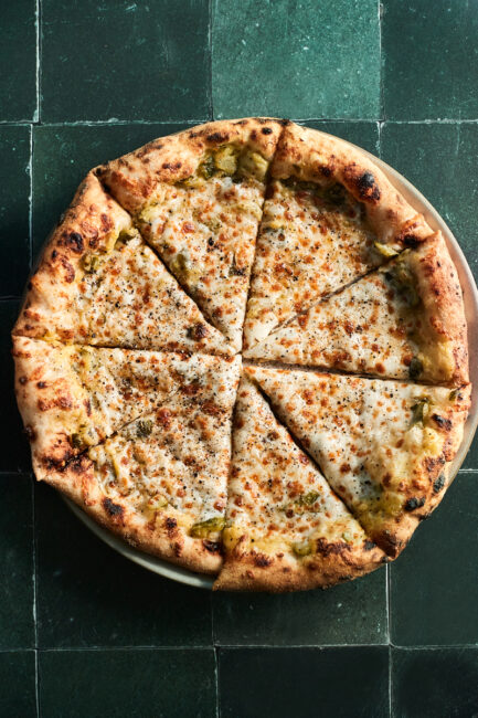 A full overhead photo of zucchini pizza on a green tile background