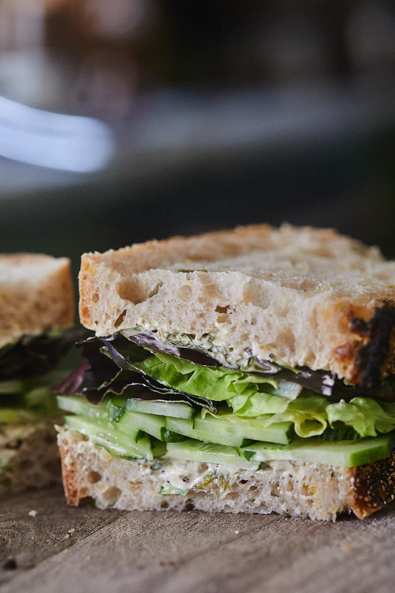 a cucumber sandwich sliced in half revealing slices of cucumber, lettuce, and a scallion cream cheese. 