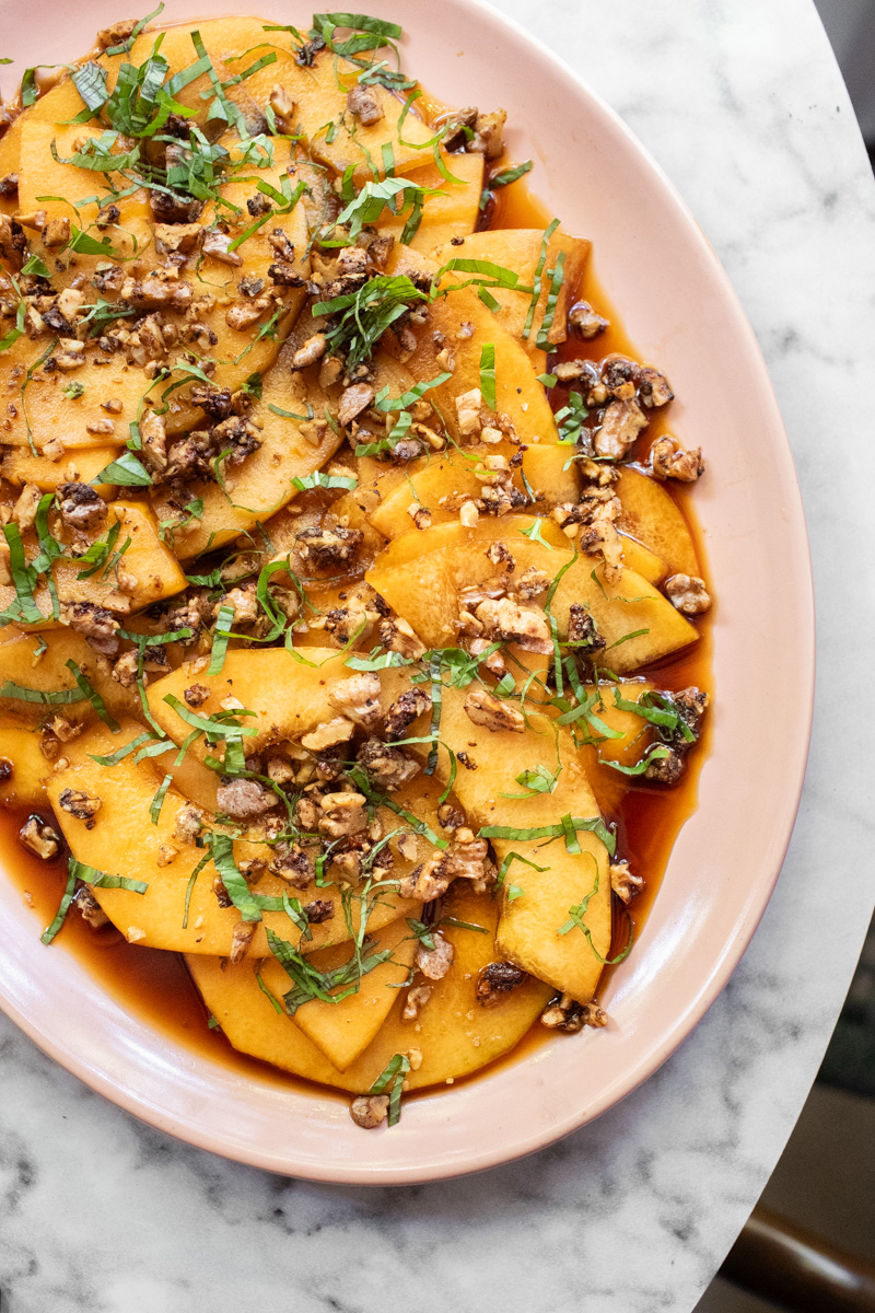 Image of marinated melon with black pepper walnuts on a pink platter. 