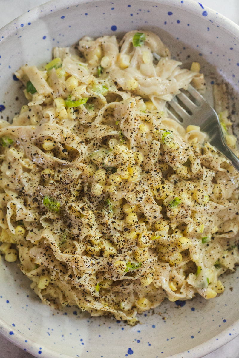 top-down photo of sweet corn pasta in a blue speckled bowl. 