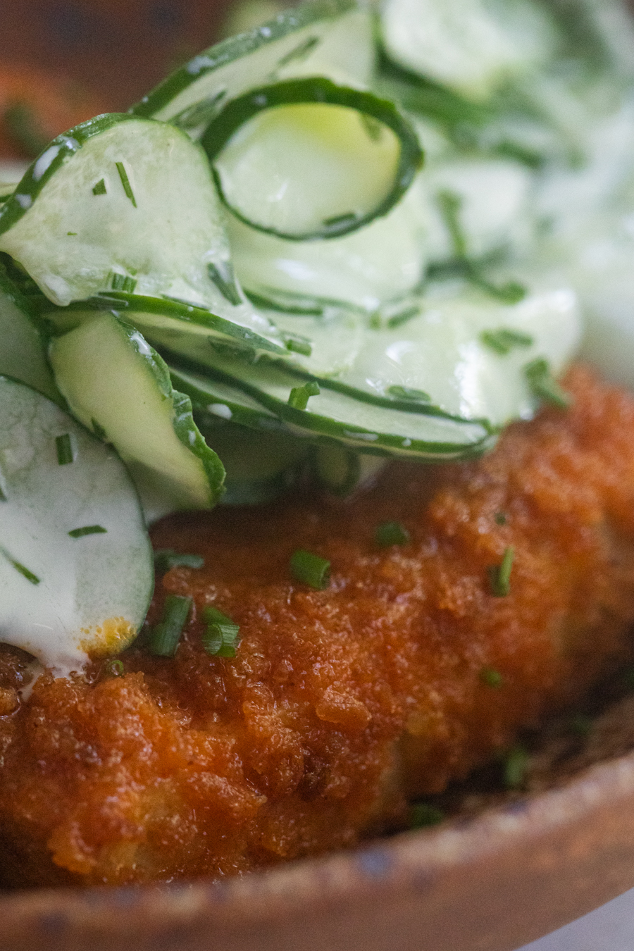 Close-up of a fried tofu cutlet tossed in buffalo sauce and topped with a cucumber salad